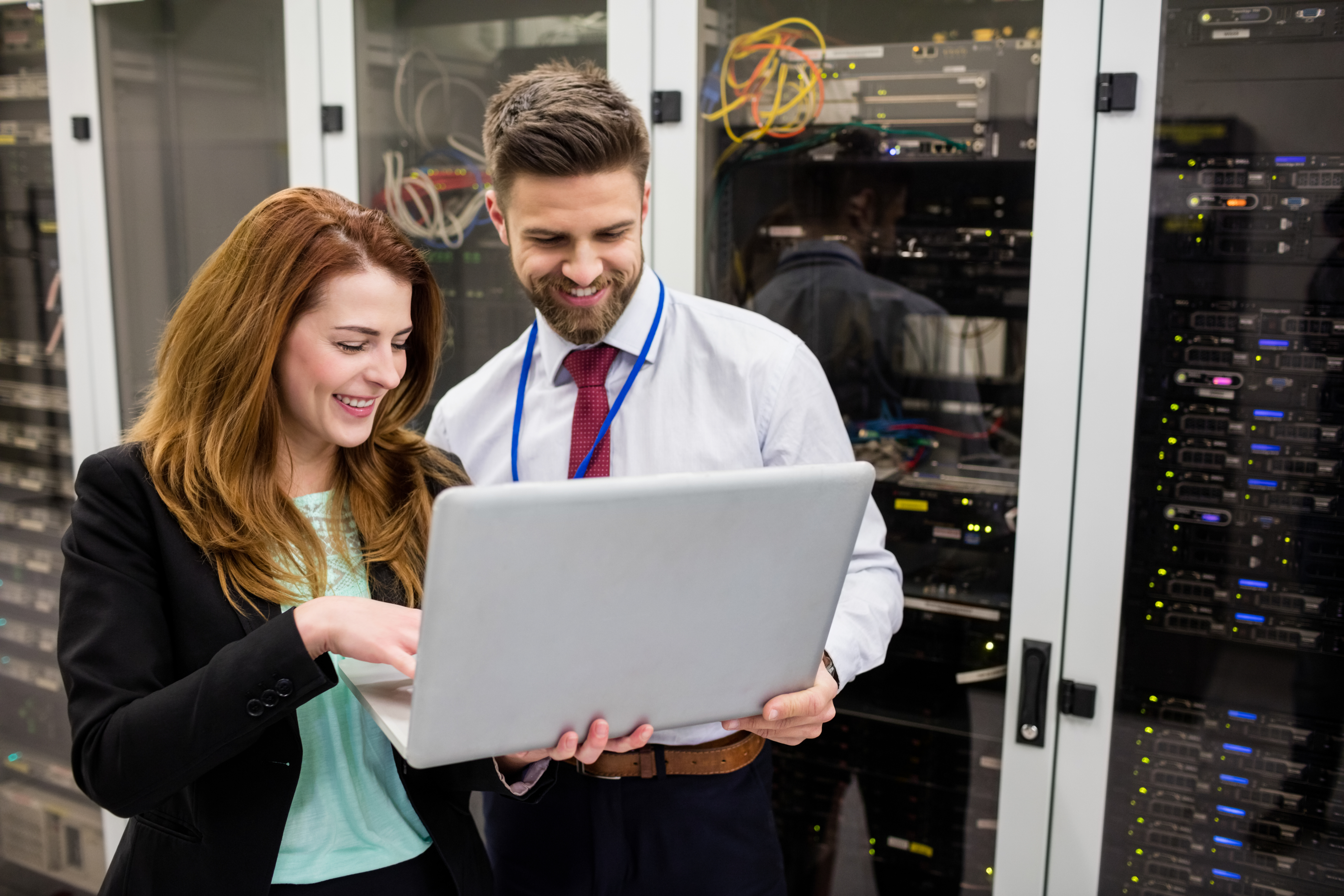 Two IT professionals reviewing work on a laptop in a server room